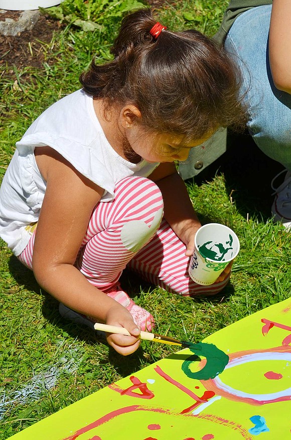 Four-year-old Janelle Perez of Nella Lane contributes to one of the colorful murals children painted on long sheets of neon green paper stretched out on the grass under the direction of the Nowodworski Foundation. 