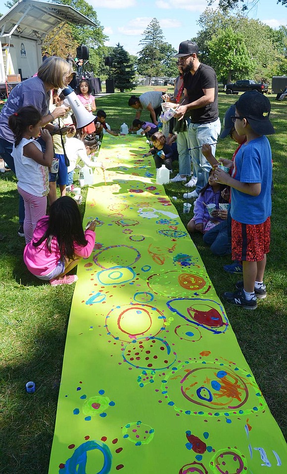 Under the direction of the Nowodworski Foundation, children have a grand time painting a colorful mural on a long sheet of neon green paper stretched out on the grass.