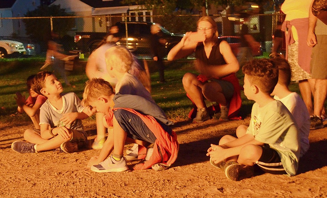 A group of kids play in the sand while their parents enjoy the fire. 