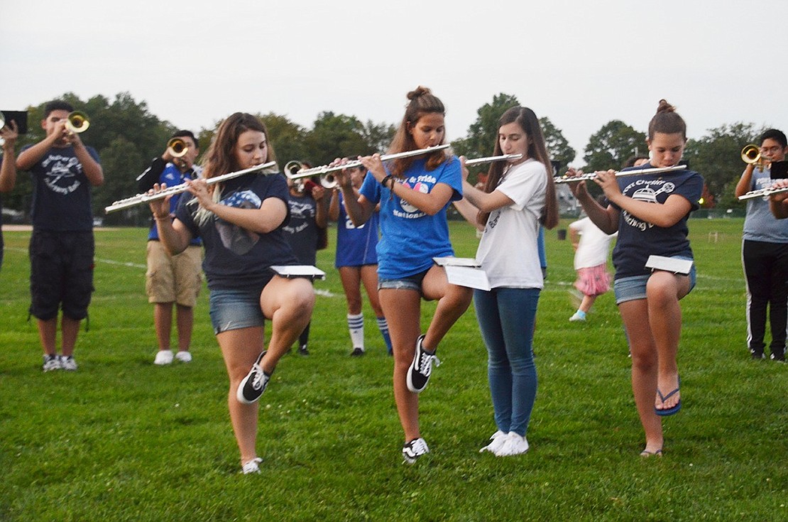 The Pride of Port Chester plays a few songs to get the crowd amped up for the bonfire. Some female flutists try to balance their music on their knees while they play. 