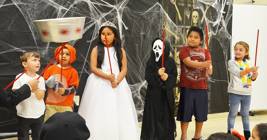 A line of kids shows off their magical balancing skills by passing a spinning bucket from stick to stick. 