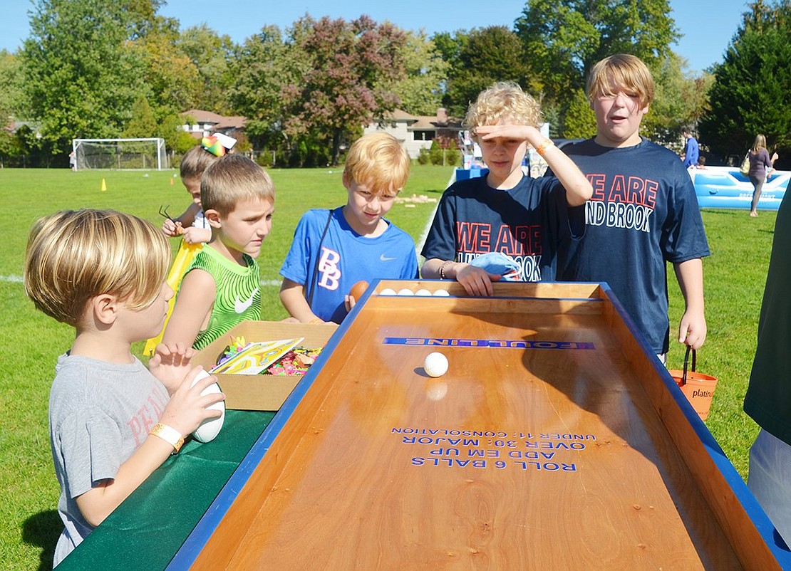 A group of boys tries to score 30 points by rolling a ball down an incline and into slots. 