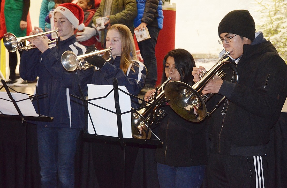 Port Chester High School Brass Ensemble members sophomore Pete Manos (left), sophomore Molly Brakewood, senior Diana Naula and sophomore Geovany Argudo play holiday melodies in front of the stage as parents take pictures of their children on Santa’s lap.