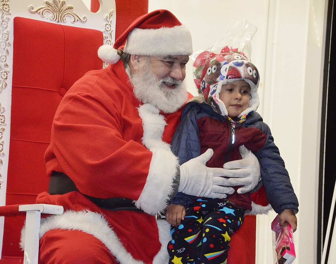 Janci Silva, a 3-year-old Port Chester resident, is happy to show Santa the Barbie toy she chose at the gift table.