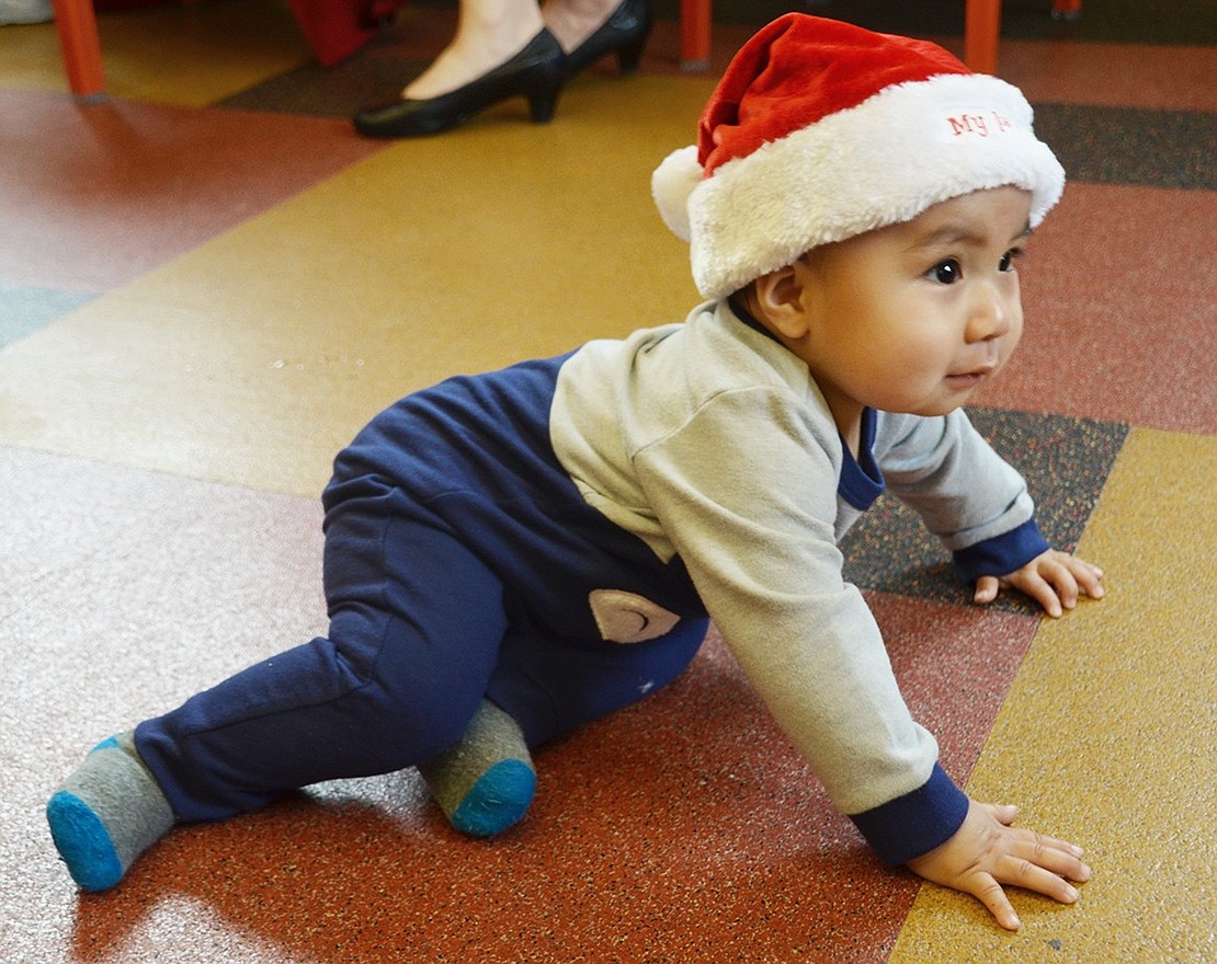 Justin Allcca, a Port Chester 9-month-old, sports his “My 1st Christmas” Santa hat as he crawls around the library. 