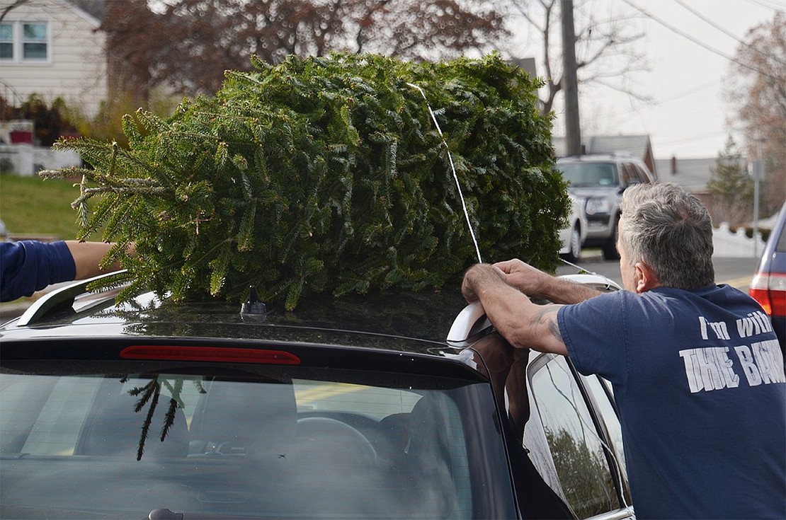 Robert Mickatavage, father of a marching band student, ties a tree on top of the car of a satisfied customer.