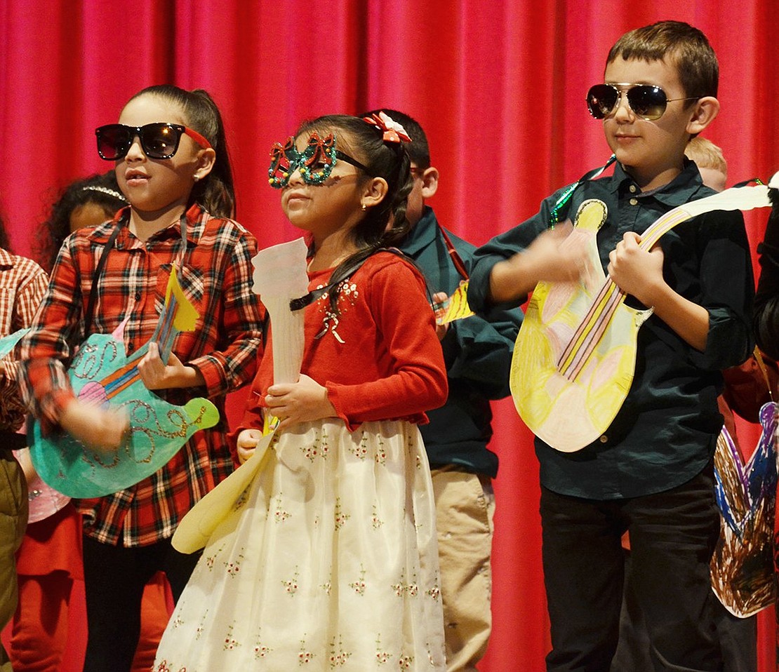 Six-year-olds Camilia Villa (left), Sophia De La Cruz and Mateo Gomez look very cool with their sunglasses and homemade guitars while rocking out to “Jingle Bell Rock.”