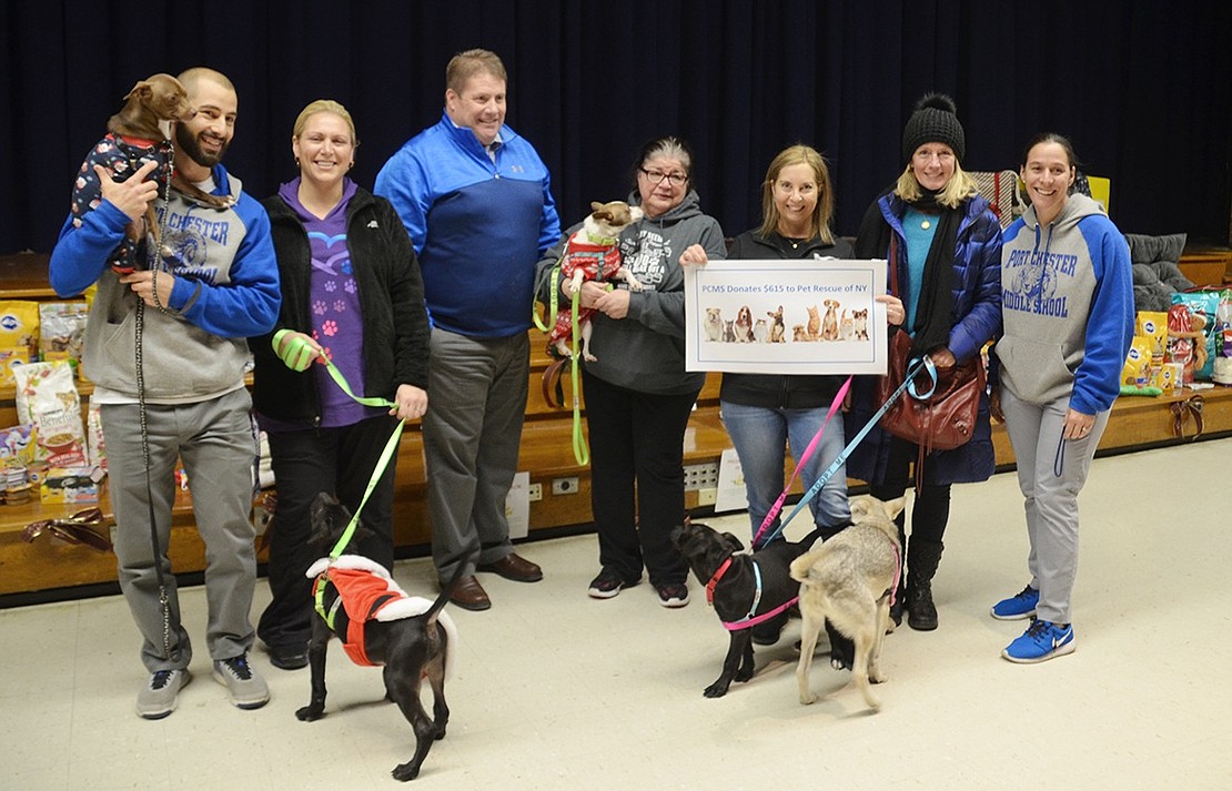 Pet Rescue associates and adoptable puppies receive a $615 honorary check and seven boxes of pet supplies from Port Chester Middle School physical education teachers Melissa Piccola (right), Michael Bonanno (left) and Principal Patrick Swift from the “Presents for Pets” fundraiser in the middle school auditorium on Thursday, Dec. 21. 