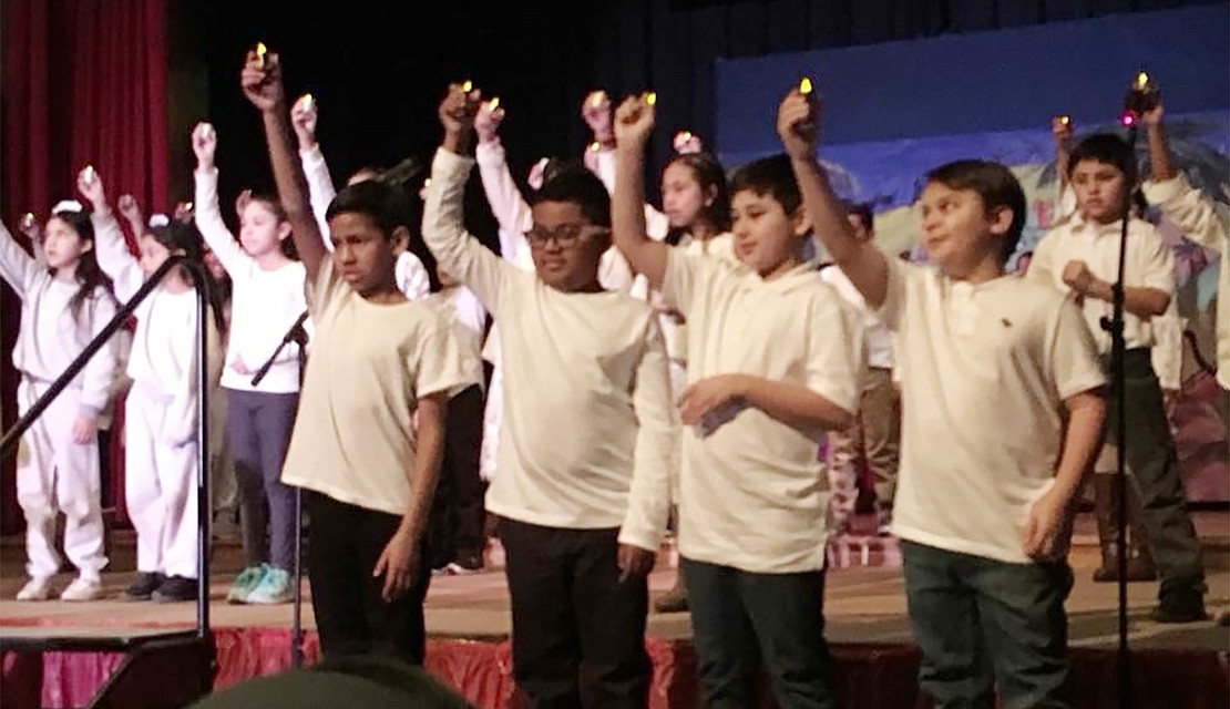 Third- and fourth-grade students hold up their lights while performing in the Christmas play. 