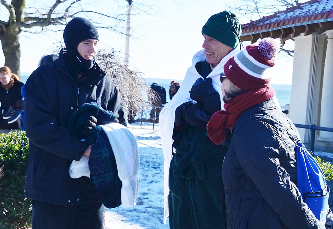 Rye resident Daniel Rudolph-Math and his 18-year-old son Tim Rudolph-Math talk with Rye resident Susanna Cronin while bundling up with blankets in an attempt to keep warm before running into freezing water.