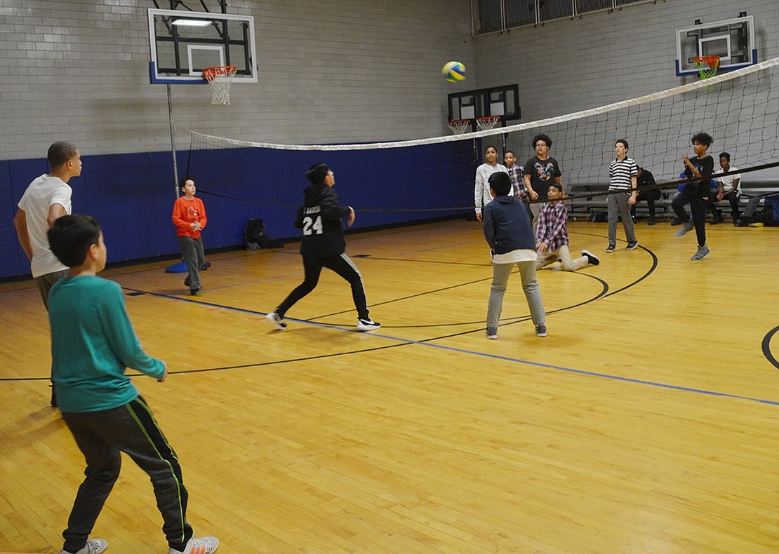 A group of kids is very invested in an intense game of volleyball in the gymnasium. 