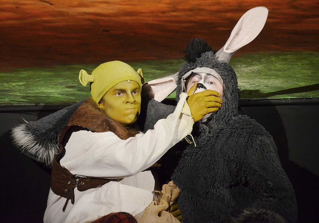 Shrek (played by Michael Lieberman) tries to keep Donkey (played by Justin Levine) quiet after they jump off stage to hide from Lord Farquaad’s guards. 