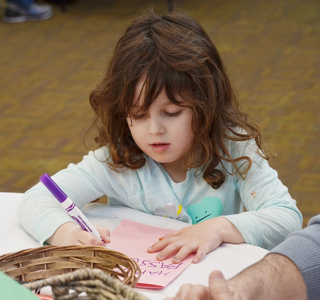 Focused on perfecting her elaborate decorations, Rye Brook resident Alexandra Spielberg, 4, carefully writes “Happy Passover” on her card for a Jewish War veteran during “Mitzvah Madness” in the Congregation KTI social hall at 575 King St. on Sunday, Mar. 18. In all, the congregation made 25 cards for the vets. 