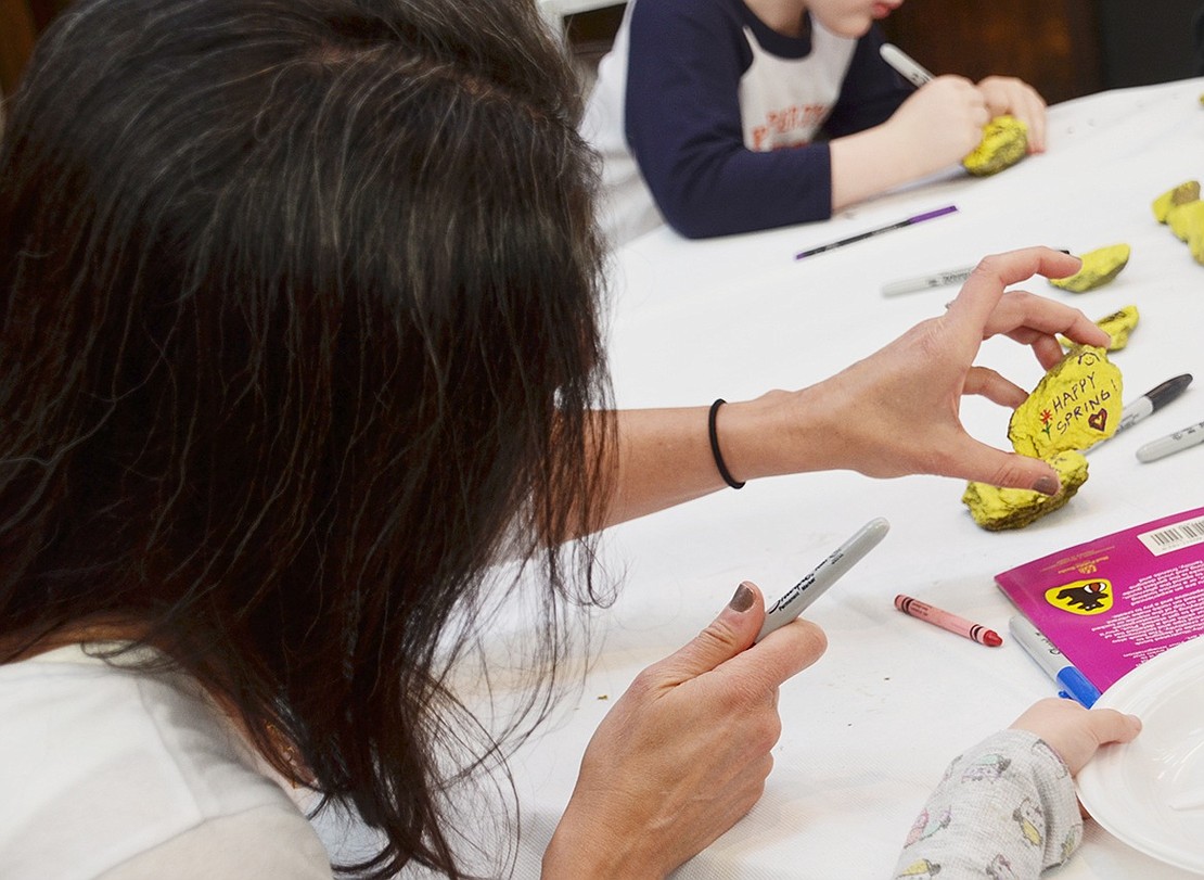 After writing “Happy Spring!” Rye Brook resident Bonnie Baker-Butler shows her kindness rock to others at the table. Festivity-goers adorned rocks with kind and positive messages to be distributed throughout the community. 