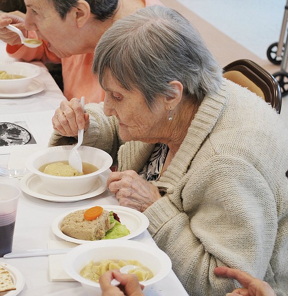 After setting aside her gefilte fish for later, Louis Court resident Carmela Bruni uses a spoon to chop her giant matzo ball into smaller pieces. 