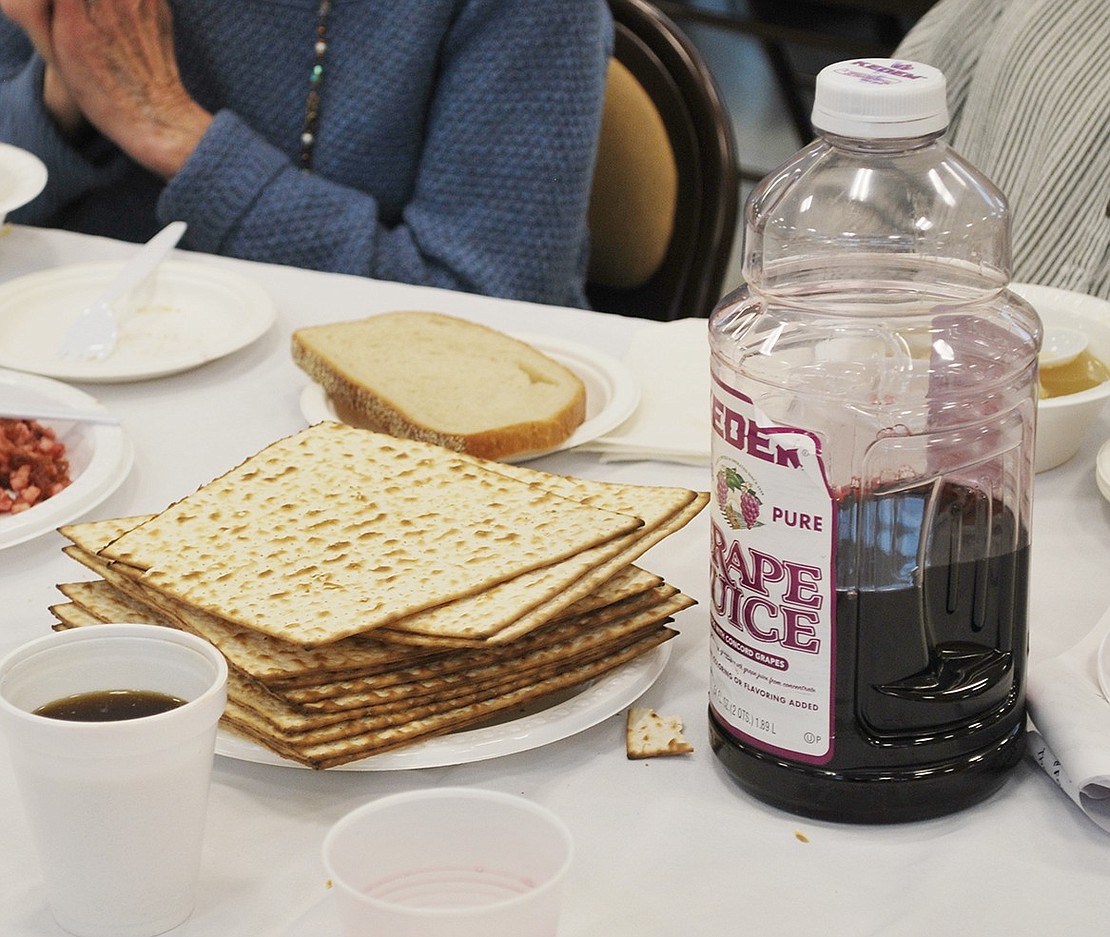 A stack of matzo and a bottle of grape juice, representing red wine, are situated at every table.