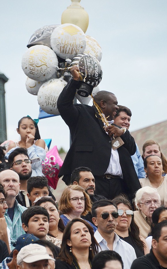With numerous balloons in hand, a proud man in the bleachers cheers on a loved one.