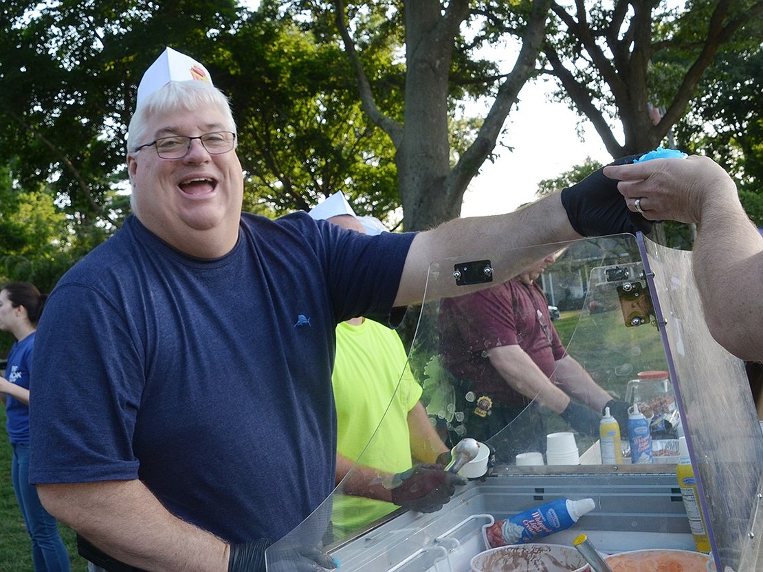 After filling a cup to the brim with ice cream, Village Administrator Chris Bradbury hands an Ice Cream Friday attendee his treat with a big smile on his face.