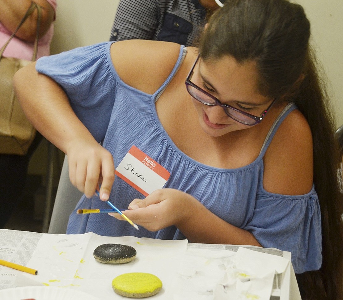 To create a sparkly effect, rising Port Chester Middle School seventh-grader Sharon Esteche taps two paint brushes together so different colored chips fall on her stone. 