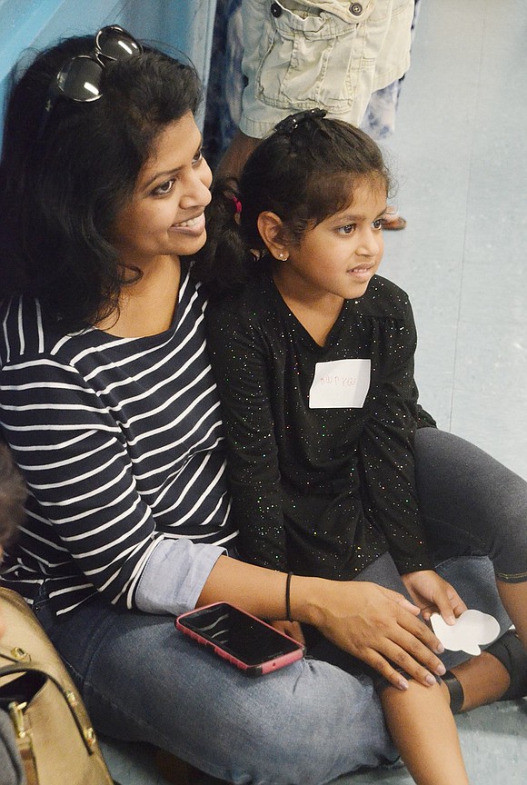 Amused by the magic show, but at a distance, North Ridge Street resident Aarya Ghosh sits on her mother Sayantani Biswas’s lap. 