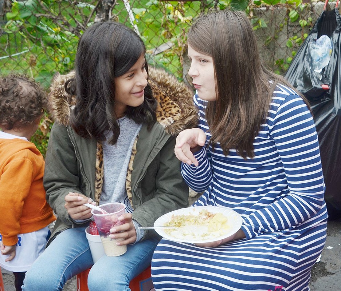 Mortimer Street resident and Corpus Christi-Holy Rosary School fifth-grader Allyson Muguerza (left) catches up with her 12-year-old friend Kendra Bobes of Greenwich, Conn. as they indulge in some traditional Peruvian food.