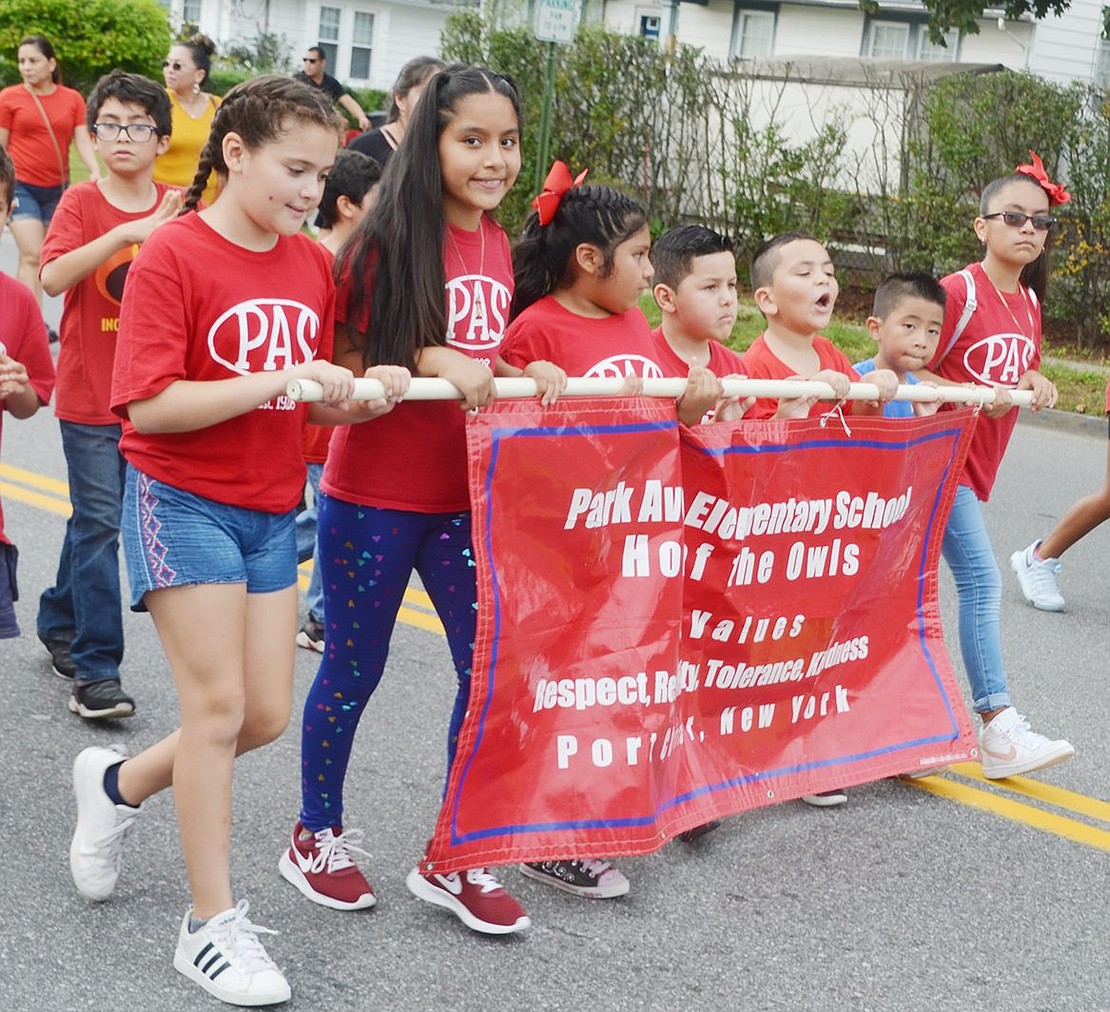 A mixed age group of students march down Westchester Avenue with the Park Avenue Elementary School banner in hand.