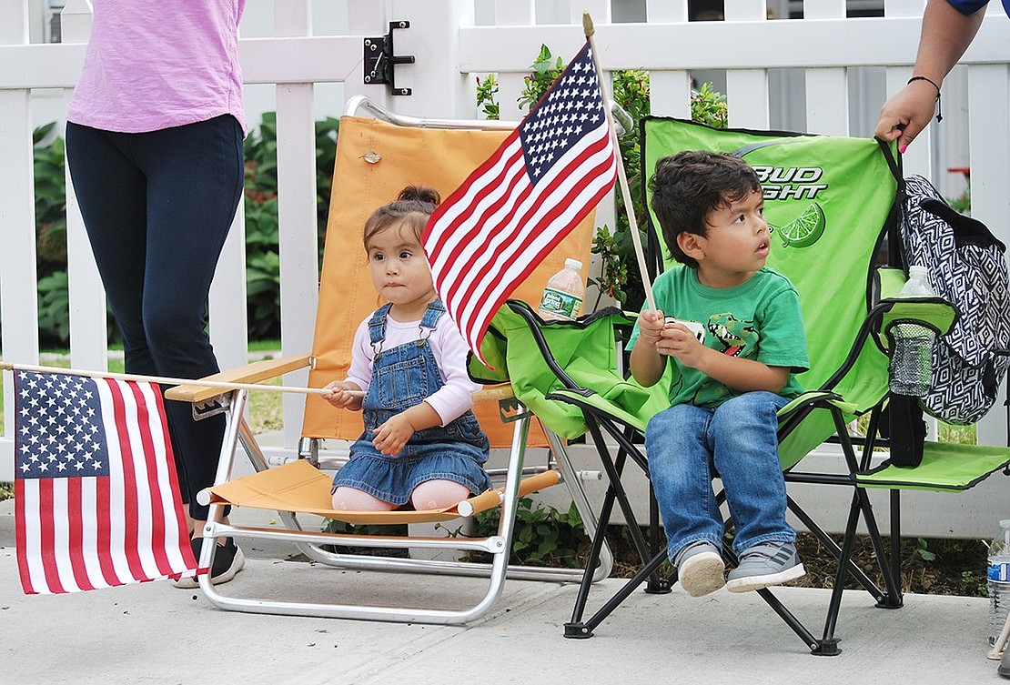 Putnam Drive residents Nina, 2, and Oliver Barrenechea, almost 4, get festive as they wave their American flags and watch the parade at the top of Westchester Avenue.