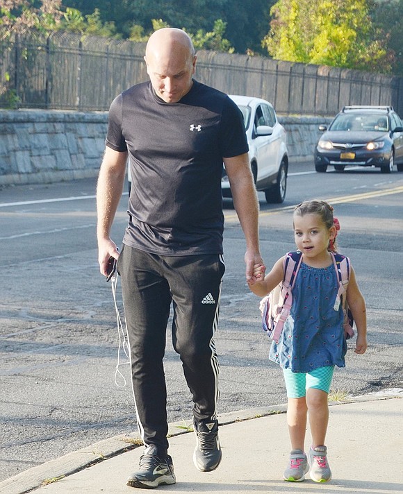 While holding hands with her father Scott, kindergartner Eleanor Pohlman flashes a coy smile on her way to school. The duo is joined by 450 other students and their families participating in the international walking day.