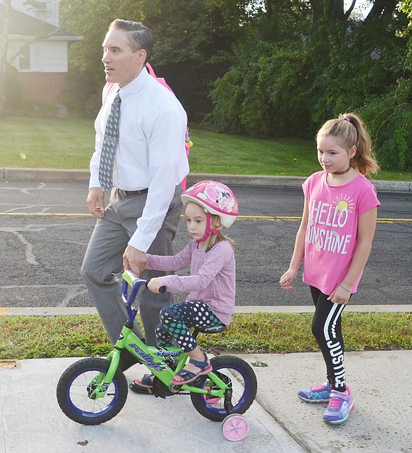 Though Julia Garofolo, 8, chose to walk, her little sister Isabella, 4, decided to take the wheels. To help his daughters, Windingwood Road resident John Garofolo joins and carries Julia’s backpack while steering Isabella’s bike.