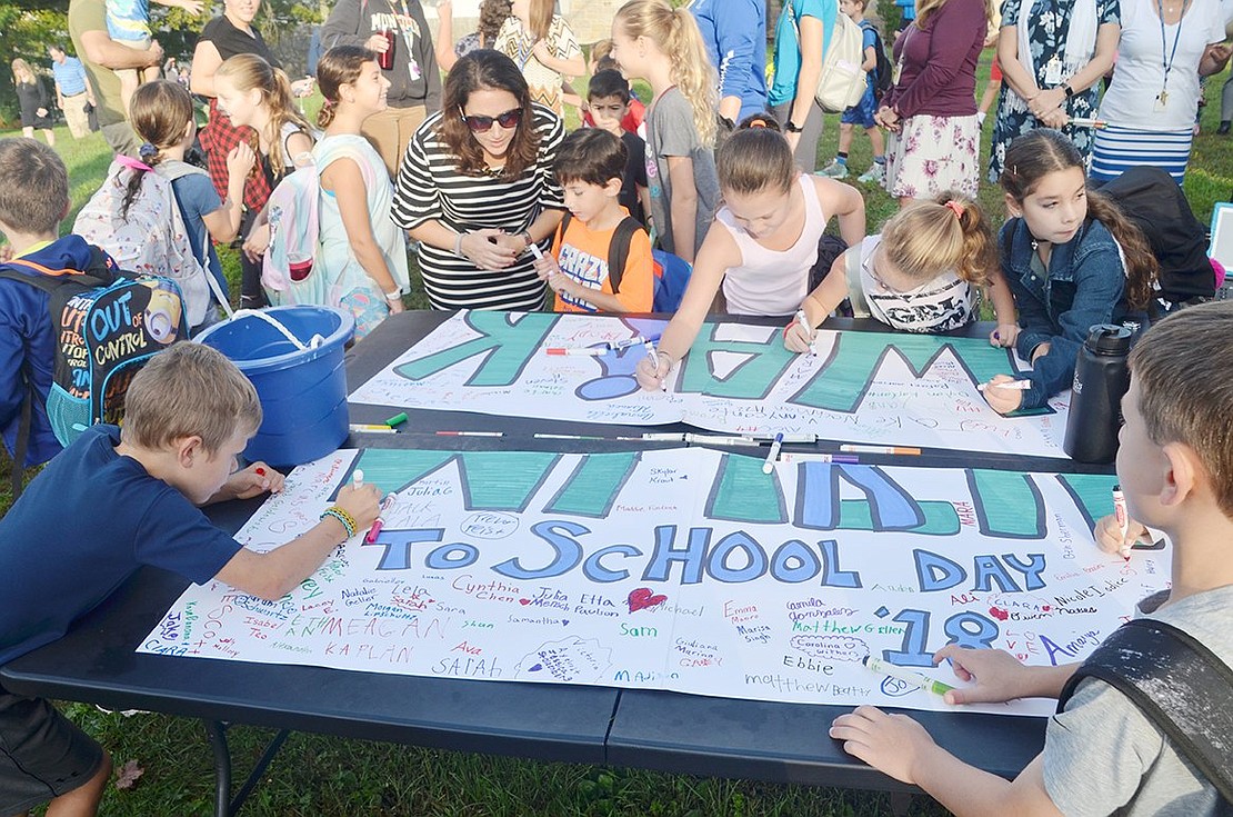 Students eagerly gather around a table greeting them at the school’s entrance to proudly sign their names on a poster after completing their morning walk.