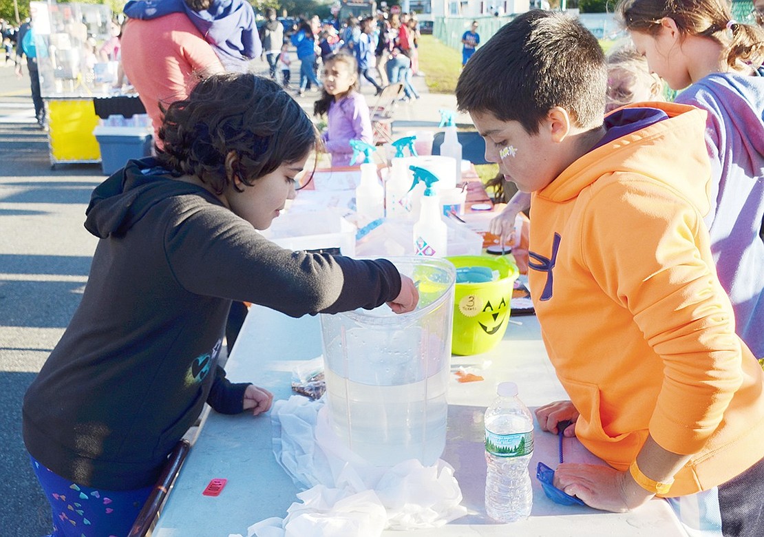 In a game to drop coins into a cup at the bottom of a jug of water, Glen Avenue resident and Park Avenue fourth-grader Amelia Jimenez carefully aims while the fifth-grader running the activity, Gage Saresky, tallies her points.