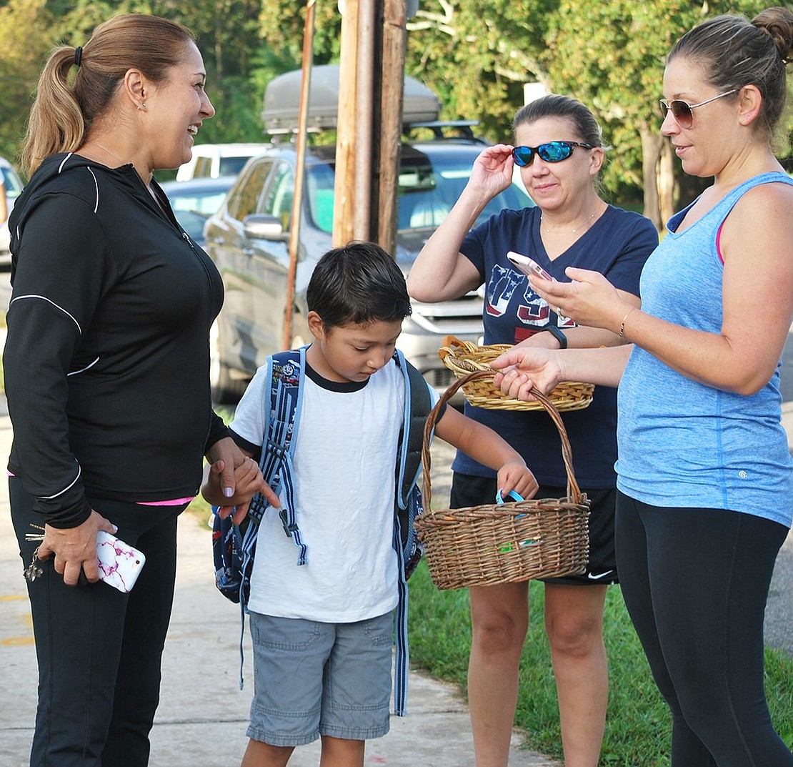 Claudia Mandujano speaks with PTA volunteers Jeanine Tobin and Allison Gilbert as her son Daniel, a kindergartner, chooses a wrist band from the basket Gilbert is holding as a reward for walking all the way from Haseco Avenue. “He enjoyed it, but he’s tired now,” said his mom.