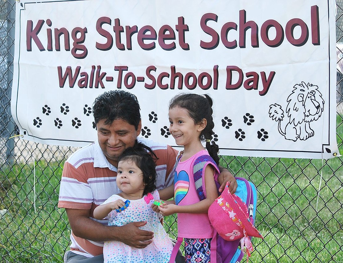 Felix Barreto poses with his children Isabella, a kindergartner, and her sister Valerie, 20 months, in front of a King Street School Walk-to-School Day sign attached to the fence on Upland Street before you round the corner and head into the school driveway. They walked six blocks from Husted Street.