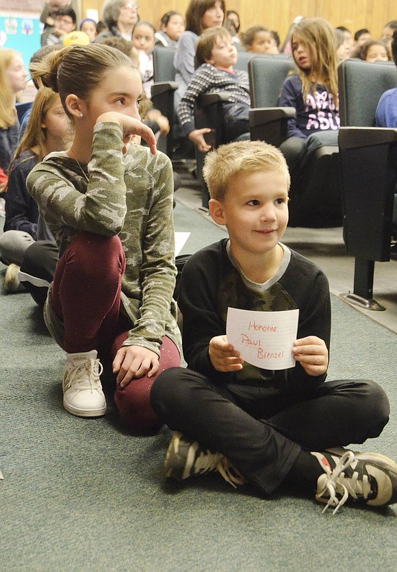 Preparing to participate in the rose giving ceremony at King Street School, first-grader Aidan Brenzel and fifth-grader Maia Scher sit in the auditorium aisle and listen to speakers.