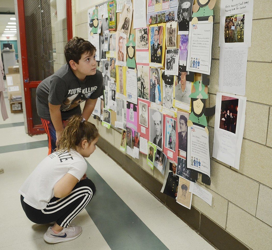 Park Avenue fourth-grader Dominick Luzzi and his third-grade sister Julianna examine photographs and profiles of veterans on a hallway wall. The collage consists of family members of teachers and staff at Park Avenue School.