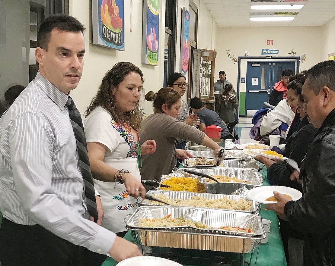 Edison Elementary School Principal Ivan Tolentino fronts the line of other helpers serving families food from the buffet. The potluck dinner featured dishes from the diverse student body families’ native countries. Courtesy of Carolee Brakewood 