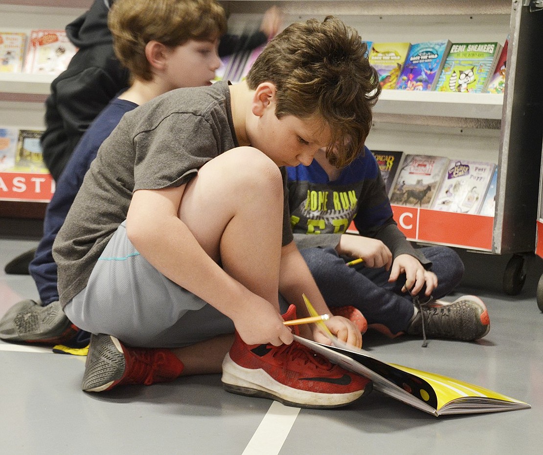 Fourth-grader Michael Colucci sits on the floor, engrossed in the reader-interactive book “Press Here” by Hervé Tullet.