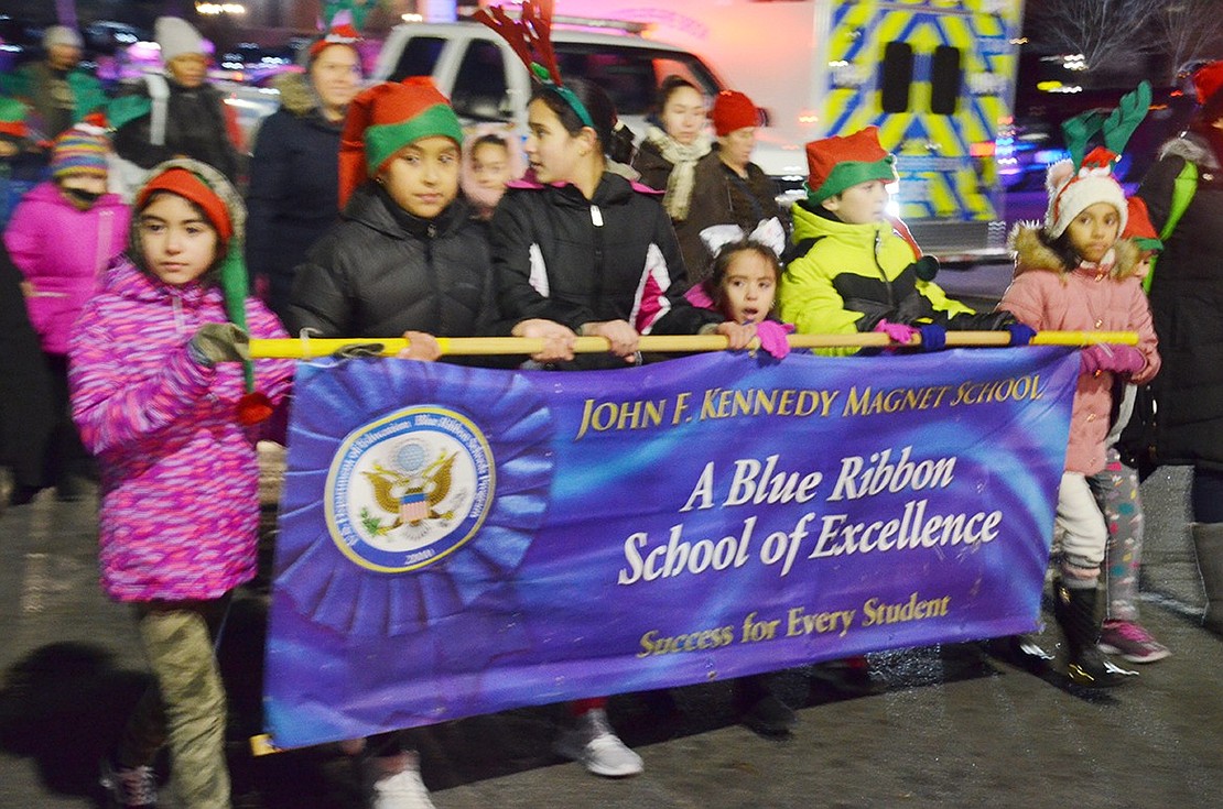 Several John F. Kennedy Elementary School students proudly clutch their school’s banner as they march down the road.