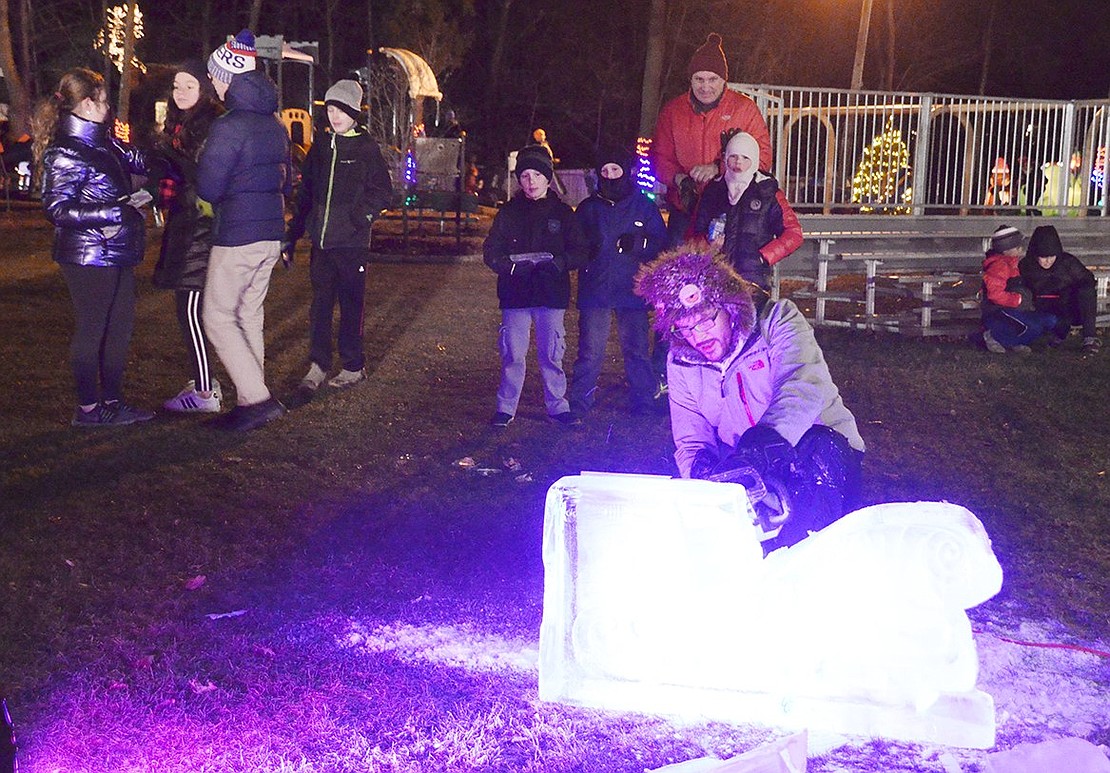 Kids of varying ages gather around ice carver Eric Wagner as he turns a block of ice into a sleigh.