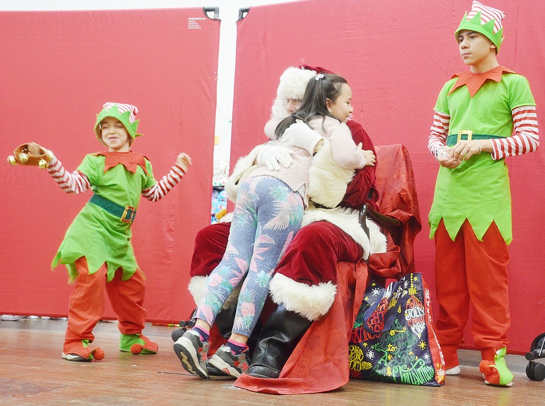 After waiting in line with hundreds of other kids at the annual Breakfast with Santa at the Don Bosco Center on Saturday, Dec. 15, Kaitlyn Salcedo’s priority is giving Santa, played by Nick Mecca, a big hug. Meanwhile, Santa’s elves Logan Massa, 7, dances to holiday music while Corpus Christi-Holy Rosary School seventh-grader Nicholas Santiago Massa waits to give the Park Avenue School second-grader candy.