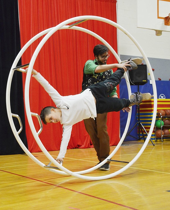 A Circus Kids Production affiliate makes sure Oliver Caspi’s feet are secure so he can safely roll across the gymnasium in the German Wheel, a new act introduced to the Blue Bird Circus this year.