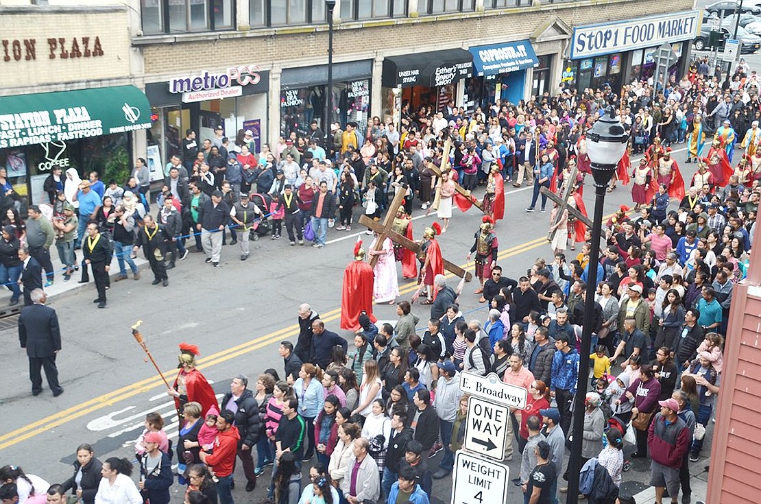 Jesus and two others bear crosses up Westchester Avenue surrounded by a throng of followers.