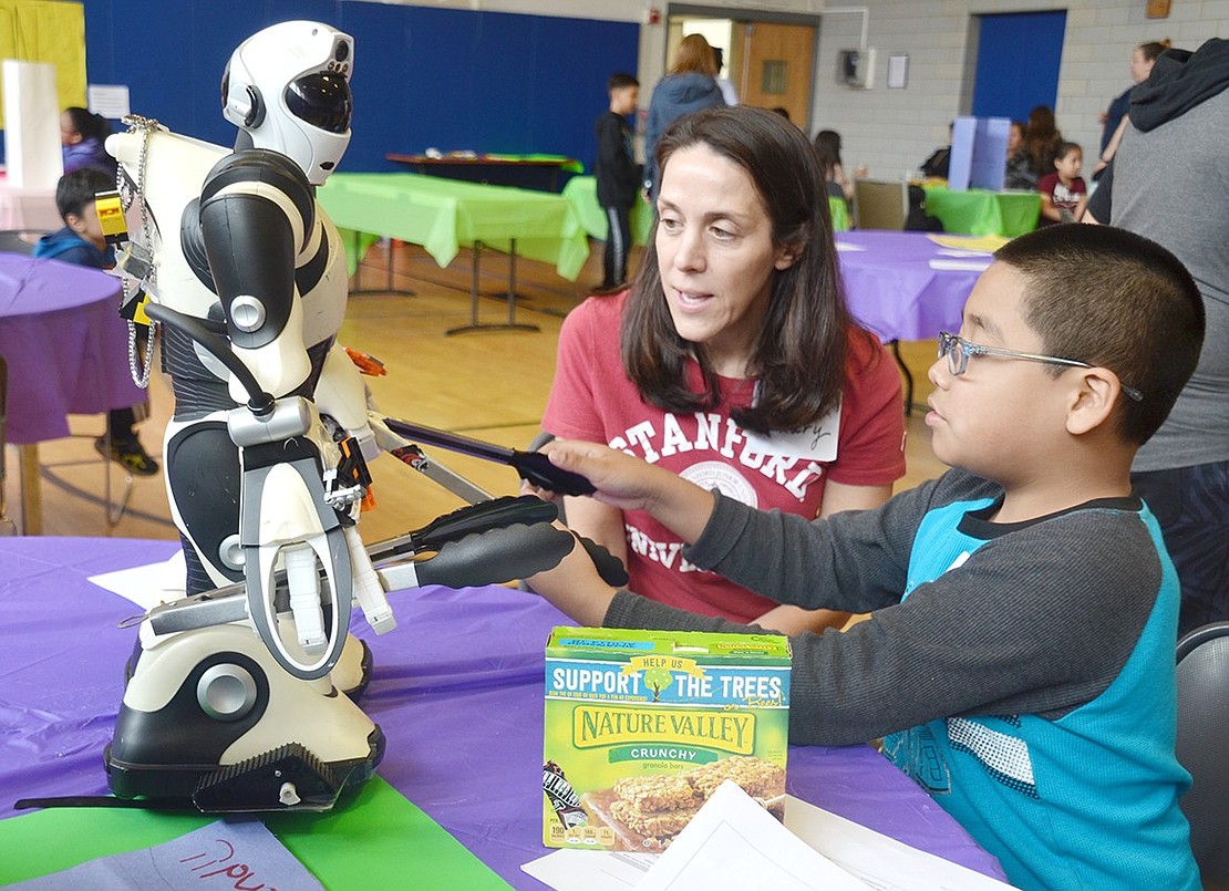 After attaching utensils to a robot’s limbs, Edison School fourth-grader Joseph Marquez shows off his Buddy Robot to Greenwich, Conn. resident Hillary Peruzzi. Peruzzi is talking to students about their creations with a half dozen other tristate-area Stanford University alumni volunteering at the Invention Convention at the Carver Center on Westchester Avenue on Saturday, Apr. 27.