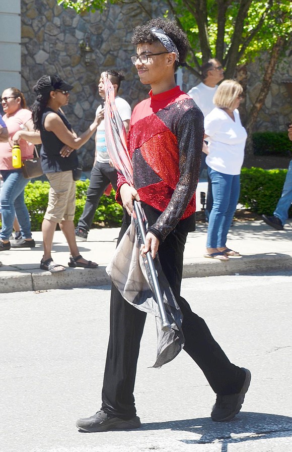 Decked out in a glitzy red and black uniform, Port Chester High School senior color guard member Zavier Garcia holds his flag is position as he marches down the street.