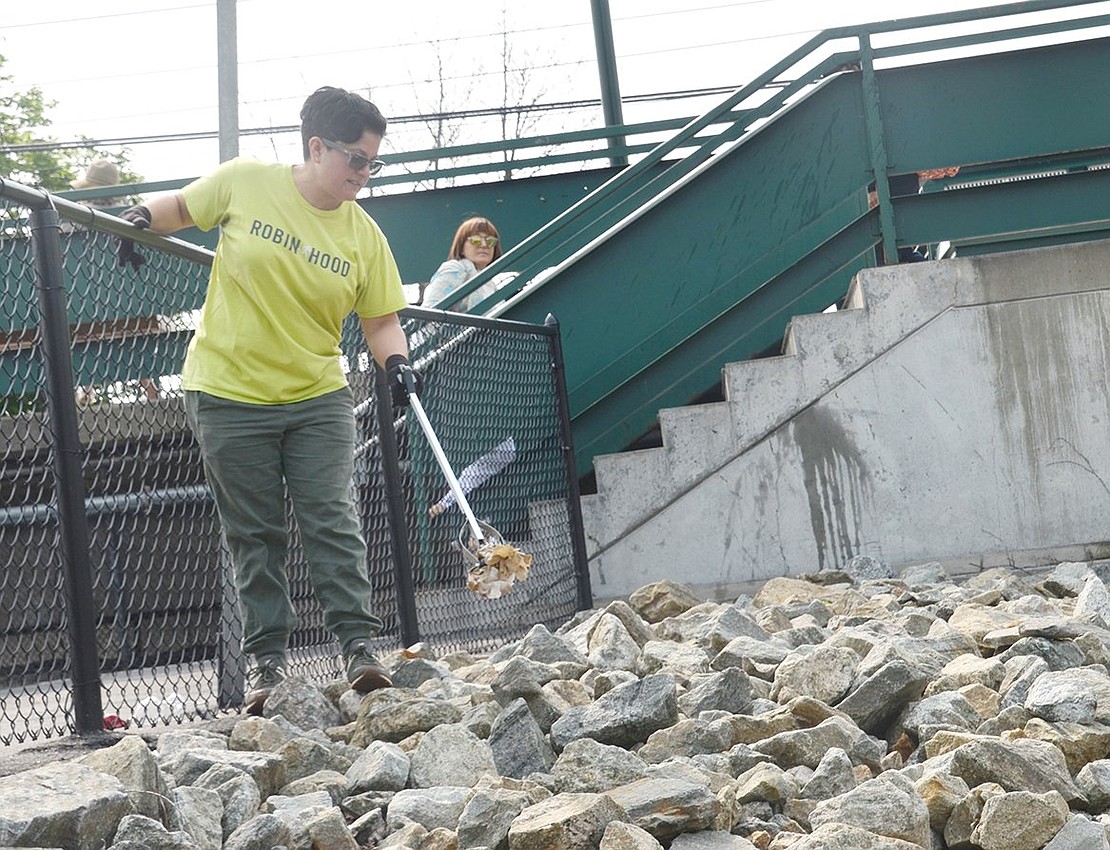 Bridgette Vassil fishes debris out from among the decorative rocks on the Westchester Avenue side of the train station Saturday morning, June 1 as part of a Clean-up Day sponsored by the Port Chester Beautification Commission.