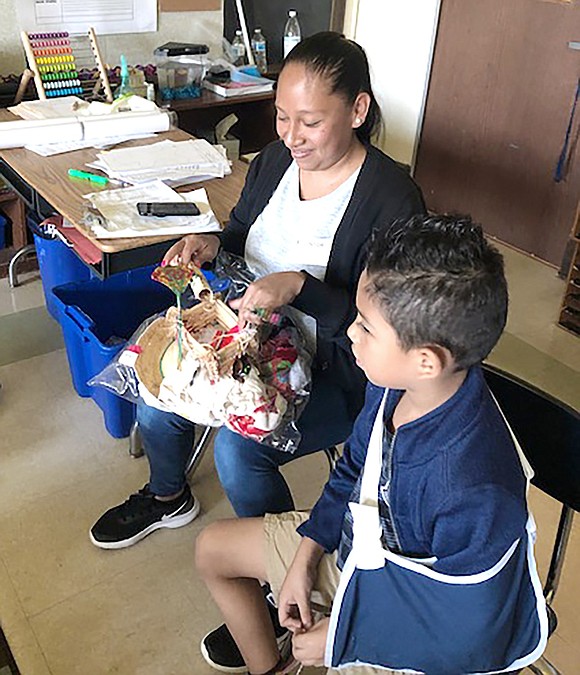 Second-grader Daniel Yanez sits with his mother Claudia Romero as she lectures about Mexican culture to Maureen Mott’s class with a physical collage of clothing, hay, fans and miniature, handcrafted pre-Hispanic palm leaves imprinted with colorful patterns.