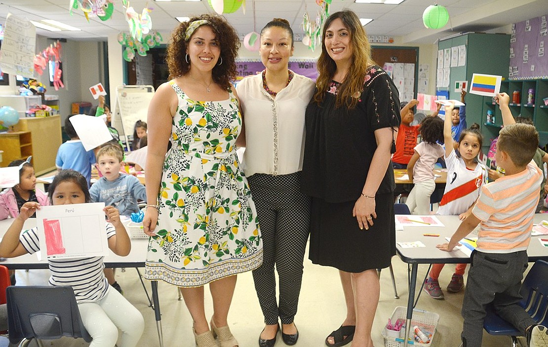 Surrounded by kindergarteners raising a vast variety of drawn flags, teacher Jessica DiGiorgi (left) and event organizers Heidi Marroquin and Jennifer Carriero-Dominguez pose for a photo.