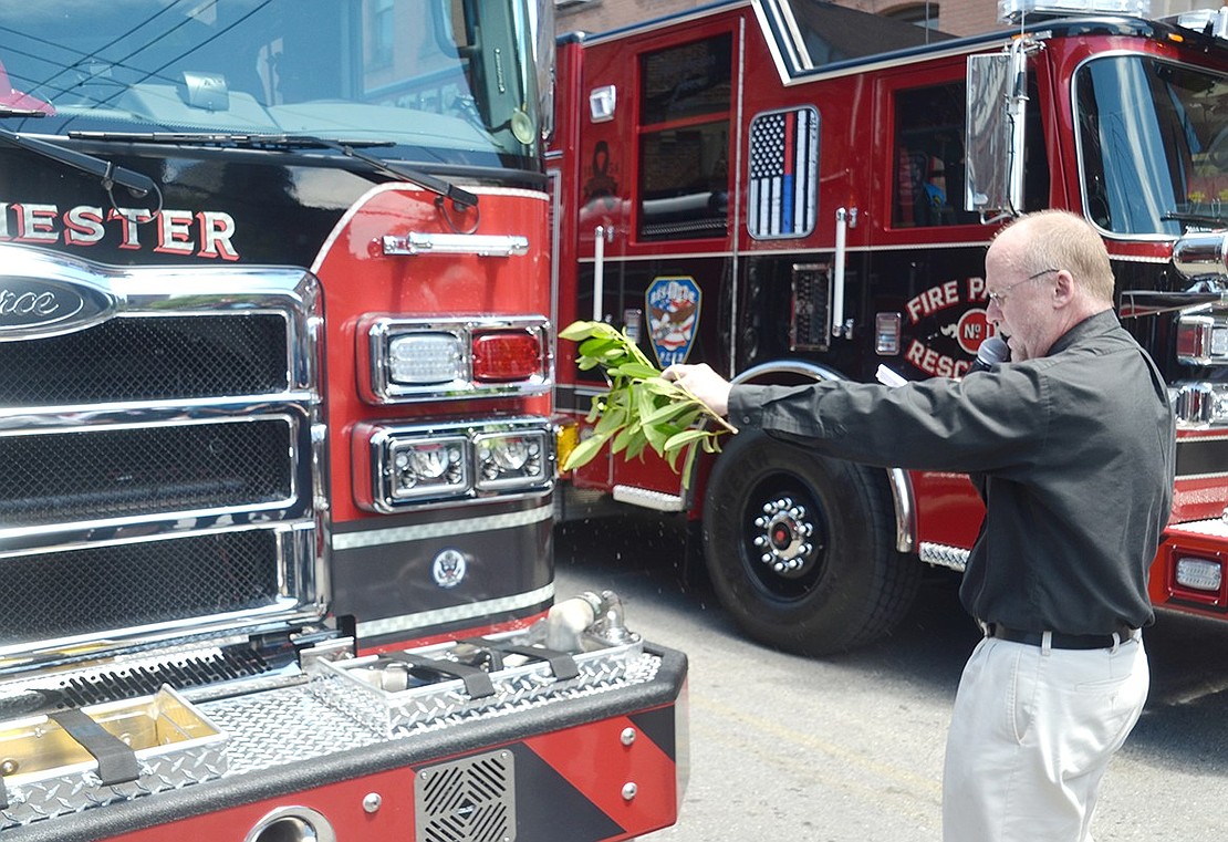 St. Paul’s Lutheran Church Pastor and Port Chester Fire Department Chaplain Jim O’Hanlon uses leaves to sprinkle water on the new fire trucks as he recites a benediction for the apparatuses and fire department.