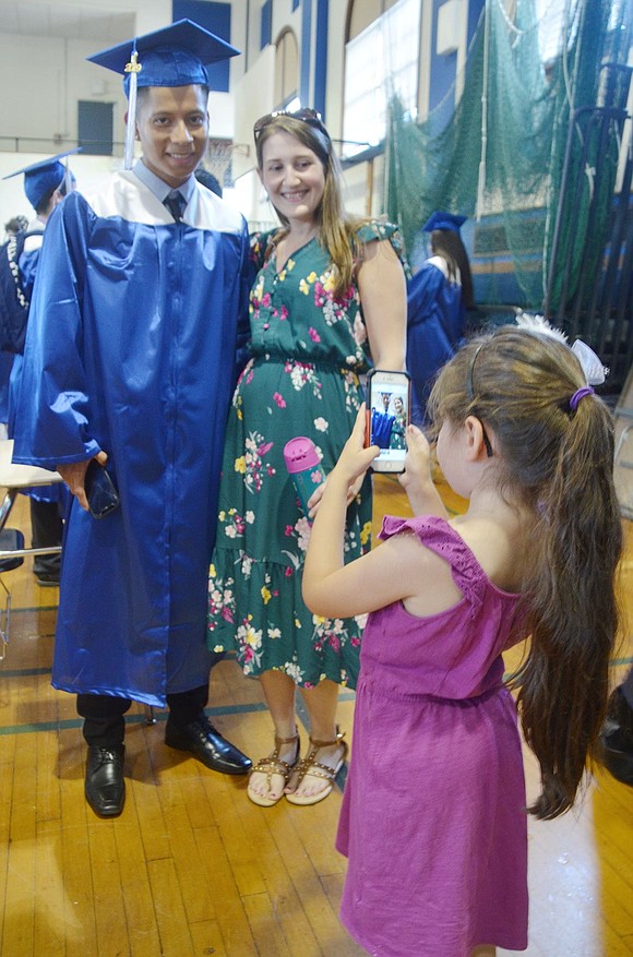 Before the ceremony, graduate Edras Lopez poses with high school English as a Second Language teacher Kathryn Zappone as her 6-year-old daughter Luna takes the picture.