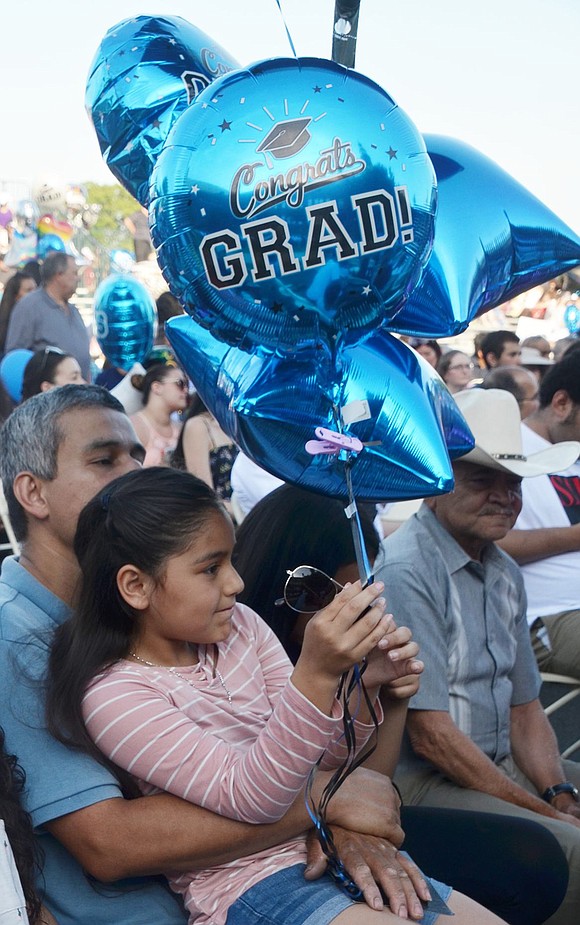 Paola Aguilar, 10, holds congratulatory balloons and sits on her father’s lap as they wait for her brother Reynaldo’s name to be called to walk across the dais.